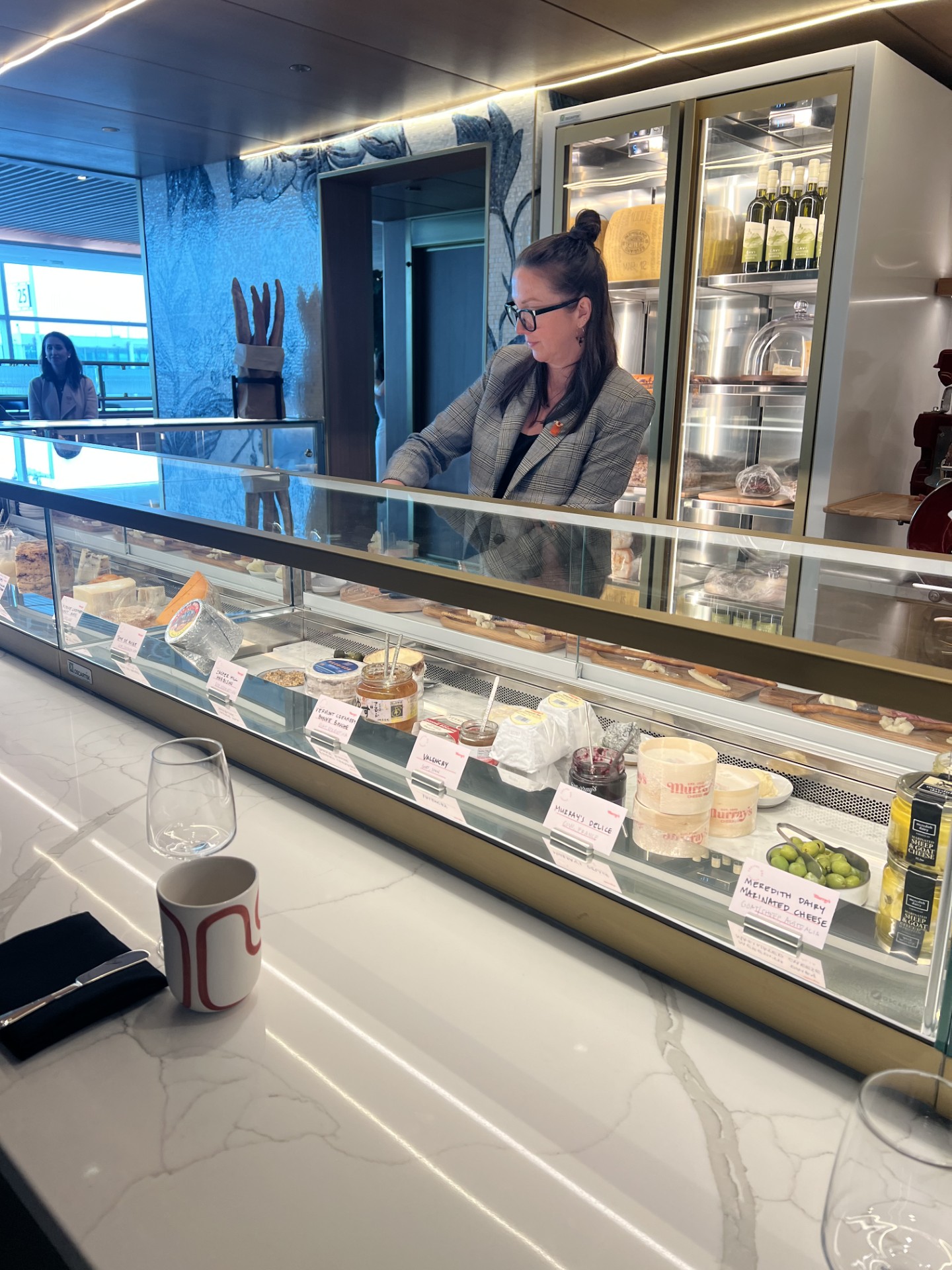 Long view of the cheese counter from Murray’s Cheese. A cheesemonger stands behind the counter preparing the tastings.